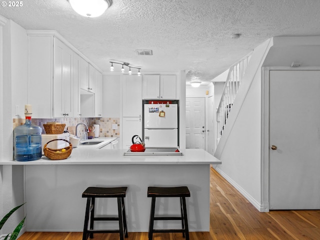 kitchen featuring a kitchen breakfast bar, kitchen peninsula, white cabinetry, and white fridge