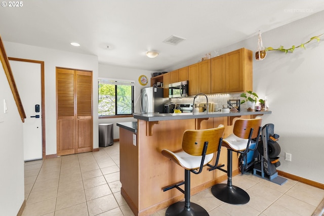 kitchen featuring tasteful backsplash, stainless steel appliances, a kitchen bar, a peninsula, and visible vents