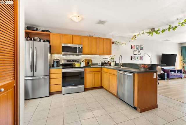 kitchen with stainless steel appliances, dark countertops, visible vents, a sink, and a peninsula