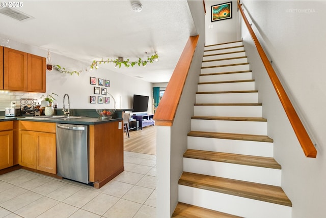 kitchen featuring a sink, dark countertops, visible vents, dishwasher, and light tile patterned floors