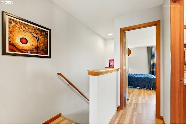 hall featuring light wood finished floors, recessed lighting, and an upstairs landing