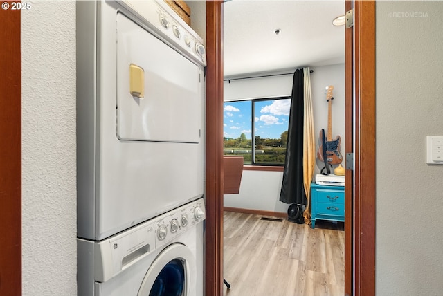 laundry room with a textured wall, stacked washer / drying machine, light wood-style floors, and laundry area