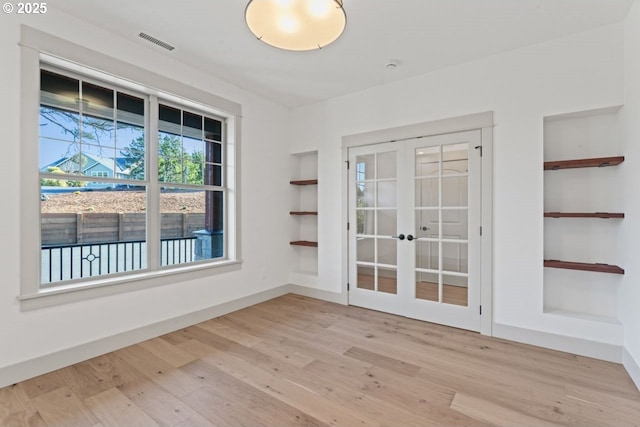 unfurnished room with built in shelves, light hardwood / wood-style flooring, and french doors