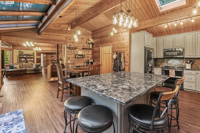 kitchen with lofted ceiling with beams, appliances with stainless steel finishes, hardwood / wood-style flooring, and a kitchen breakfast bar