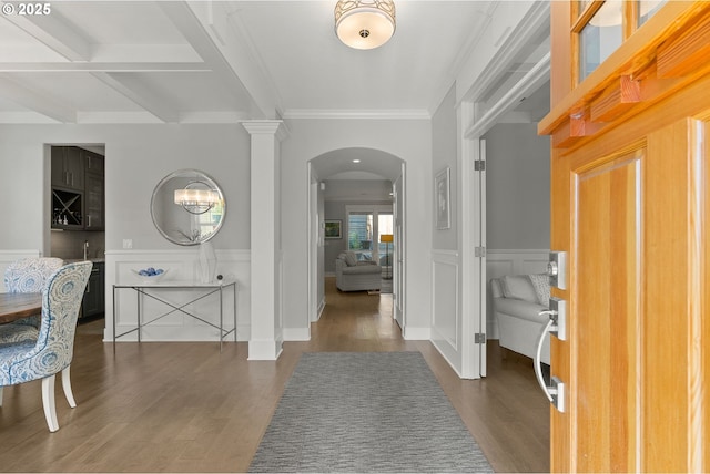 foyer entrance featuring arched walkways, wood finished floors, crown molding, wainscoting, and a decorative wall