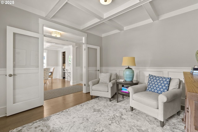sitting room with coffered ceiling, wood finished floors, beam ceiling, and a wainscoted wall