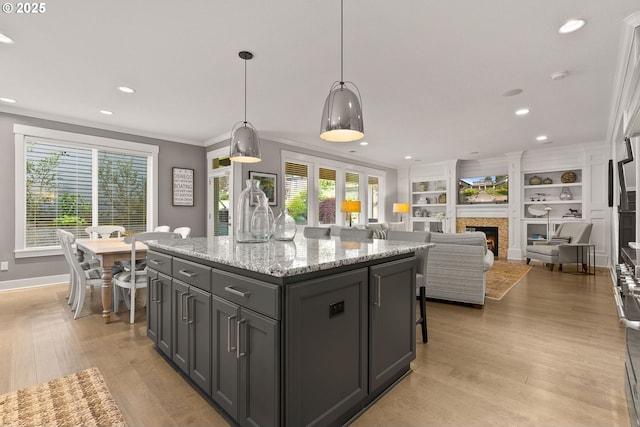 kitchen with light wood finished floors, baseboards, a lit fireplace, recessed lighting, and a kitchen island