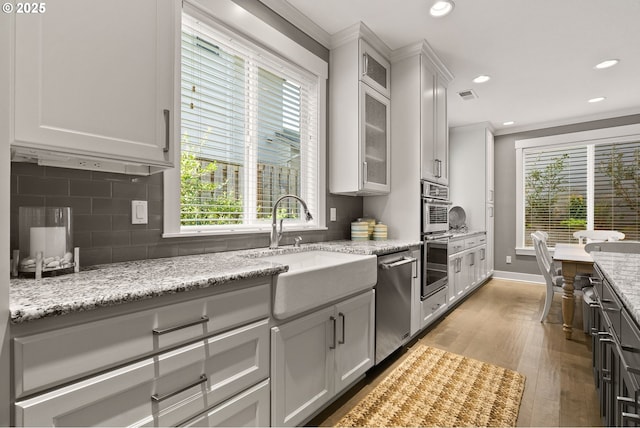 kitchen with stainless steel dishwasher, a sink, backsplash, light wood-style flooring, and crown molding