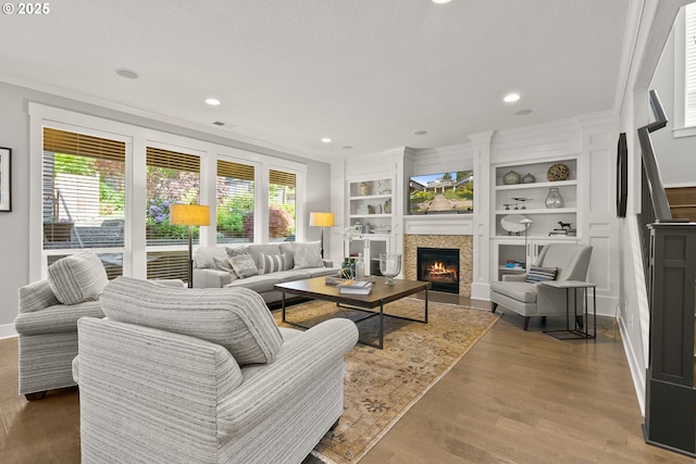 living room with ornamental molding, a lit fireplace, wood finished floors, built in features, and recessed lighting