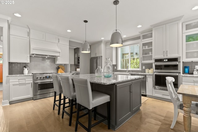 kitchen featuring appliances with stainless steel finishes, tasteful backsplash, custom exhaust hood, white cabinetry, and crown molding