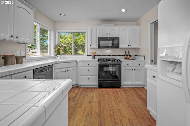 305 SW 169th Pl, Beaverton, OR 97006 - kitchen featuring black appliances, tile countertops, a sink, white cabinets, and light wood-style floors