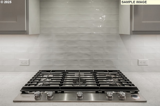kitchen view of stainless steel gas cooktop, gray cabinetry, and backsplash