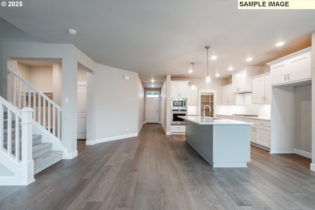 kitchen with appliances with stainless steel finishes, a sink, wood finished floors, baseboards, and white cabinets