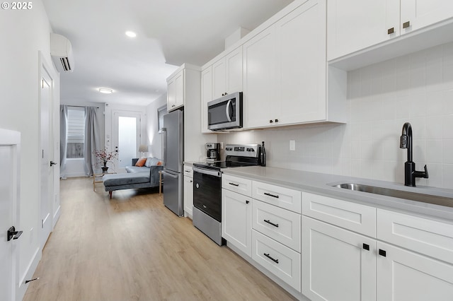 kitchen with white cabinets, sink, light wood-type flooring, appliances with stainless steel finishes, and a wall unit AC