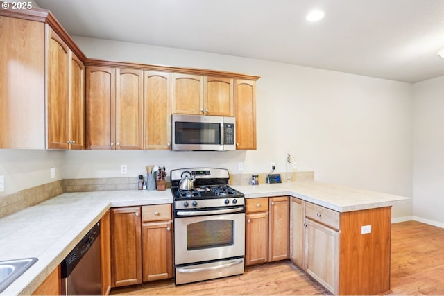 kitchen with sink, stainless steel appliances, light hardwood / wood-style flooring, and kitchen peninsula