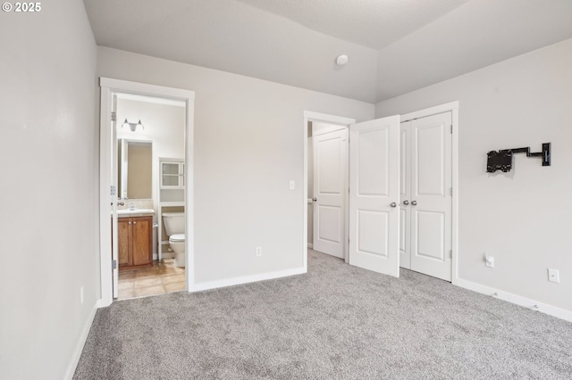 unfurnished bedroom with sink, ensuite bathroom, vaulted ceiling, a closet, and light colored carpet