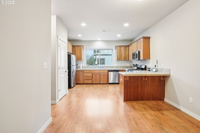 kitchen featuring appliances with stainless steel finishes, light hardwood / wood-style flooring, a kitchen bar, and kitchen peninsula