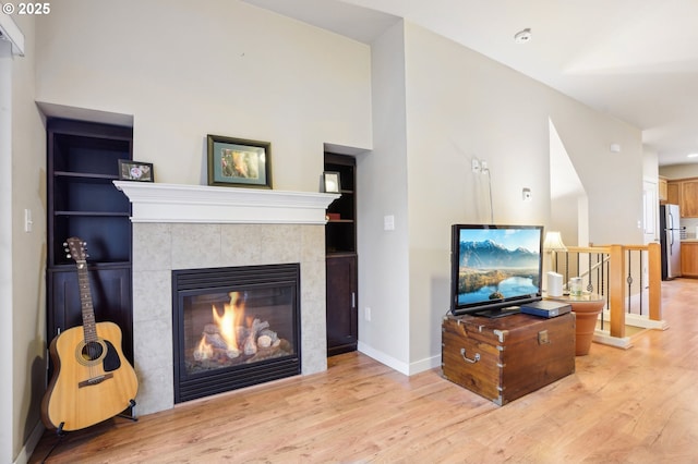 living room featuring a tiled fireplace, light wood-type flooring, and built in shelves