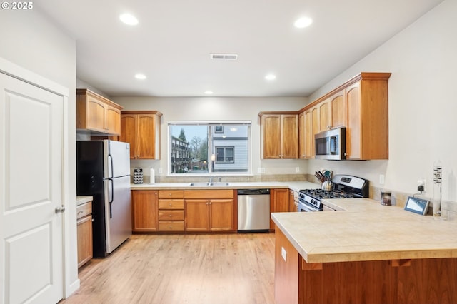 kitchen featuring sink, light hardwood / wood-style flooring, kitchen peninsula, and appliances with stainless steel finishes