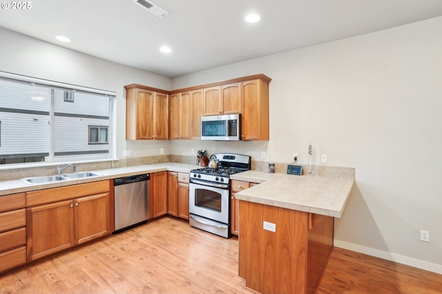 kitchen with sink, light wood-type flooring, kitchen peninsula, and appliances with stainless steel finishes