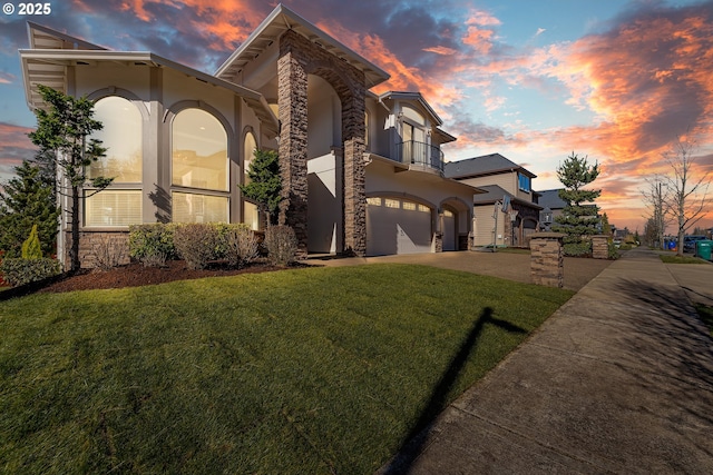 view of front of home featuring an attached garage, a balcony, concrete driveway, stucco siding, and a front lawn