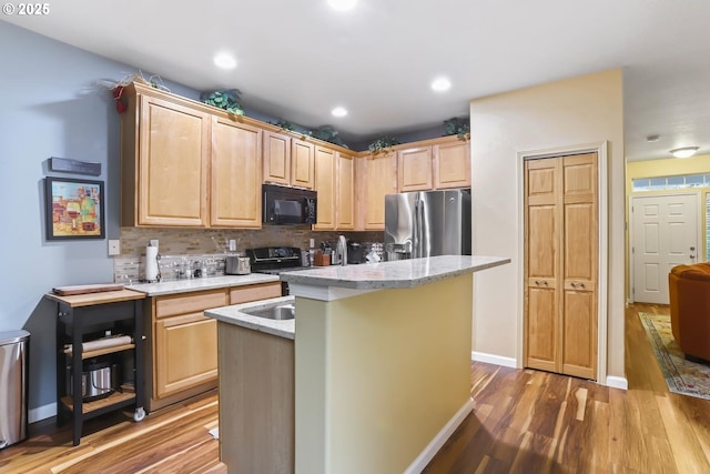 kitchen featuring light brown cabinets, backsplash, light hardwood / wood-style floors, a center island with sink, and black appliances