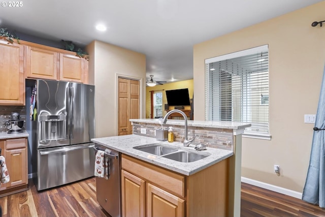 kitchen with appliances with stainless steel finishes, sink, ceiling fan, light stone counters, and a center island with sink