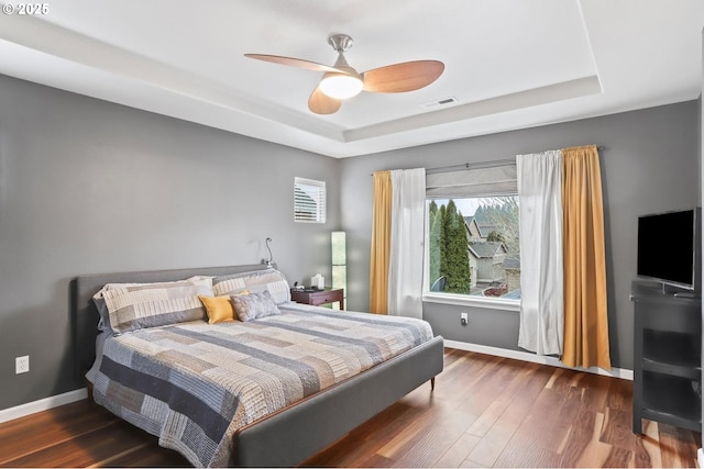 bedroom with ceiling fan, a tray ceiling, and dark hardwood / wood-style flooring