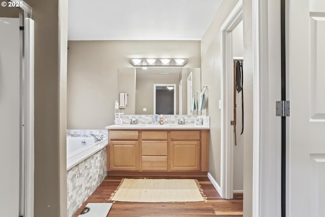 bathroom featuring wood-type flooring, tiled tub, and vanity