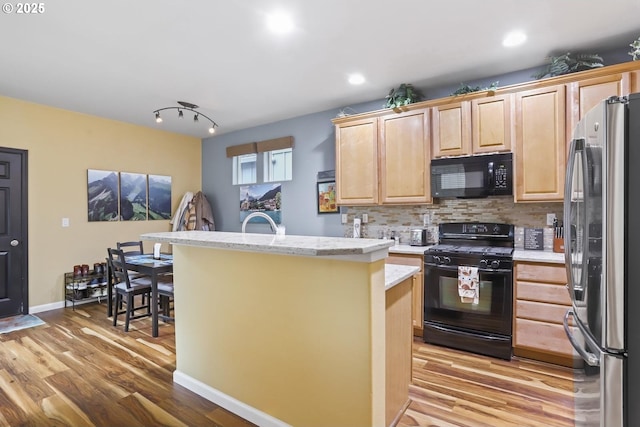 kitchen with black appliances, light hardwood / wood-style floors, decorative backsplash, a center island with sink, and a breakfast bar area