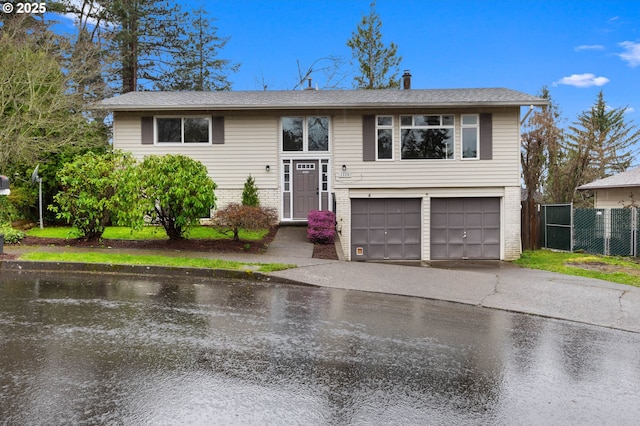 split foyer home with brick siding, aphalt driveway, a garage, and fence