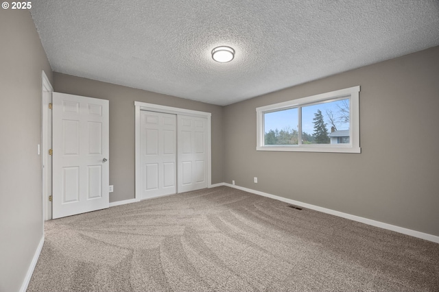 unfurnished bedroom featuring visible vents, baseboards, carpet floors, a closet, and a textured ceiling