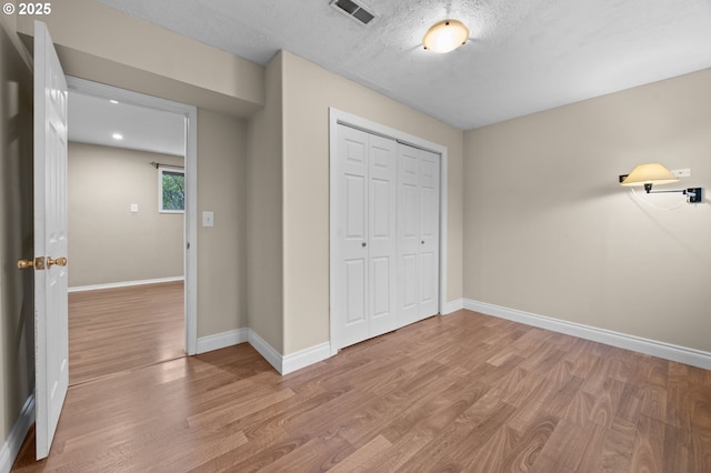 unfurnished bedroom with light wood finished floors, visible vents, baseboards, a closet, and a textured ceiling