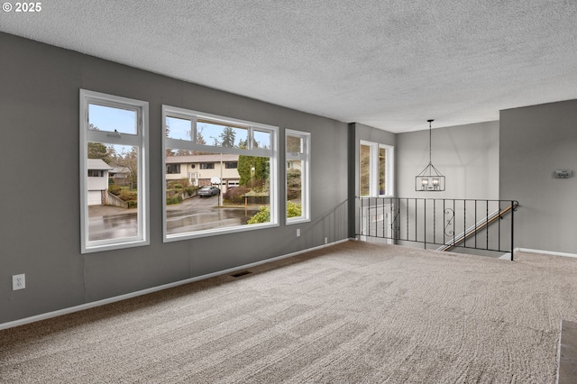 carpeted empty room featuring an inviting chandelier, visible vents, baseboards, and a textured ceiling