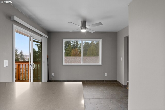 tiled empty room featuring a ceiling fan and baseboards