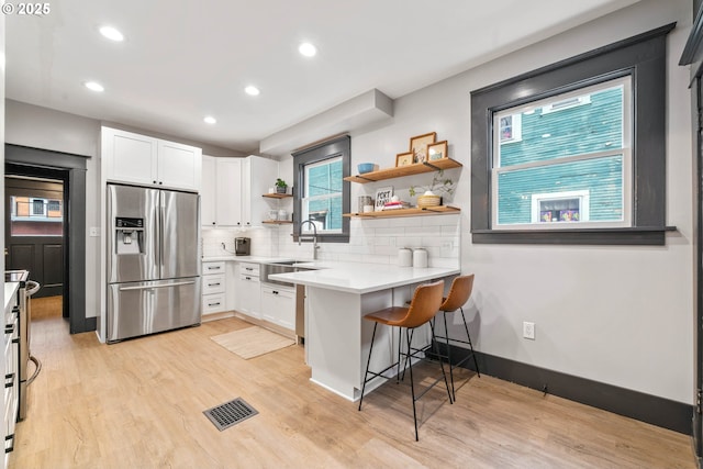 kitchen with backsplash, white cabinets, stainless steel fridge, kitchen peninsula, and a breakfast bar area