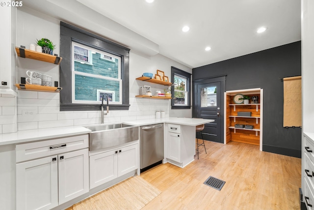 kitchen with dishwasher, backsplash, sink, a kitchen bar, and white cabinetry