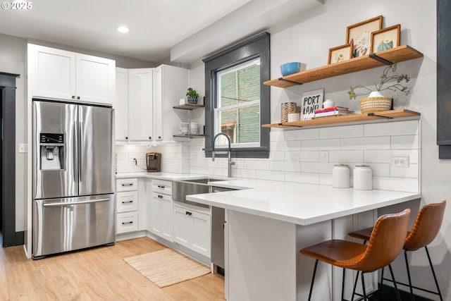 kitchen with white cabinets, a kitchen breakfast bar, sink, stainless steel refrigerator with ice dispenser, and light hardwood / wood-style floors