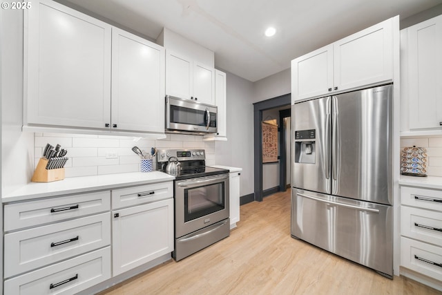 kitchen featuring light wood-type flooring, backsplash, stainless steel appliances, and white cabinetry