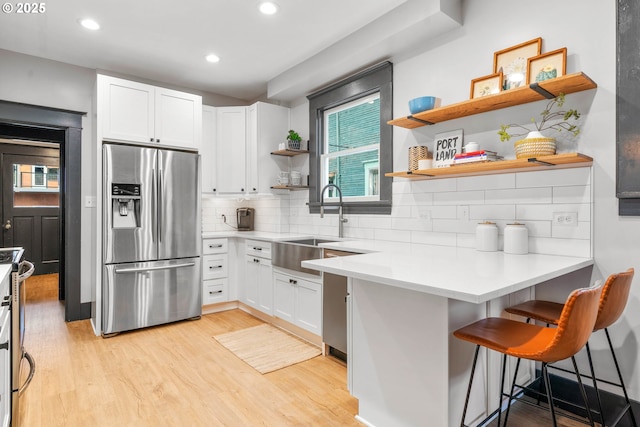 kitchen featuring stainless steel fridge, a kitchen bar, decorative backsplash, white cabinets, and light wood-type flooring