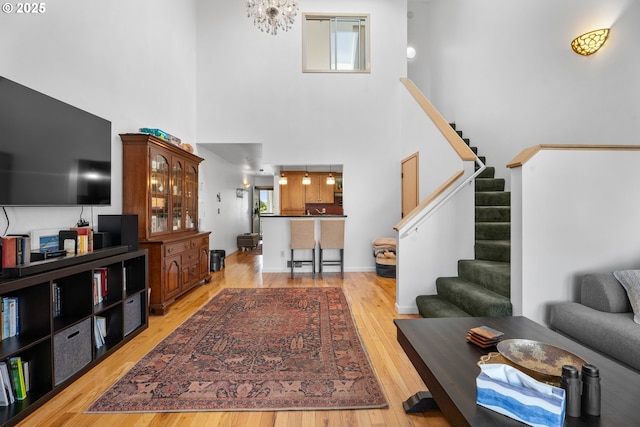 living area with light wood-style floors, stairway, a high ceiling, plenty of natural light, and a chandelier
