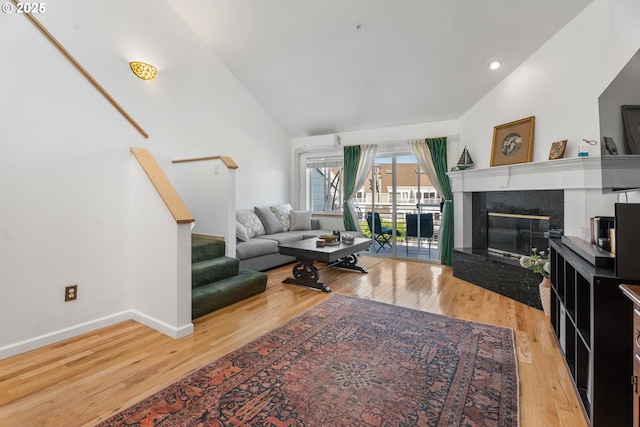 living area featuring wood finished floors, a high end fireplace, baseboards, stairs, and high vaulted ceiling