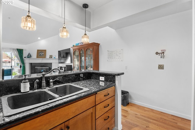 kitchen with a sink, light wood-style flooring, brown cabinets, pendant lighting, and baseboards