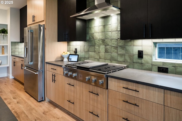 1006 S 48th Pl, Ridgefield, WA 98642 - kitchen featuring appliances with stainless steel finishes, wall chimney exhaust hood, tasteful backsplash, light wood finished floors, and dark countertops