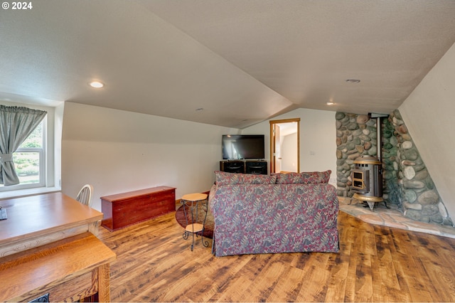 living room featuring a textured ceiling, a wood stove, wood-type flooring, and vaulted ceiling