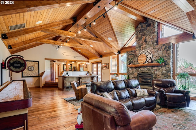 living room with rail lighting, light hardwood / wood-style flooring, wooden ceiling, vaulted ceiling with beams, and a stone fireplace