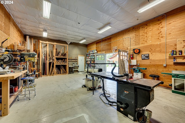 miscellaneous room with a workshop area, concrete floors, and wooden walls