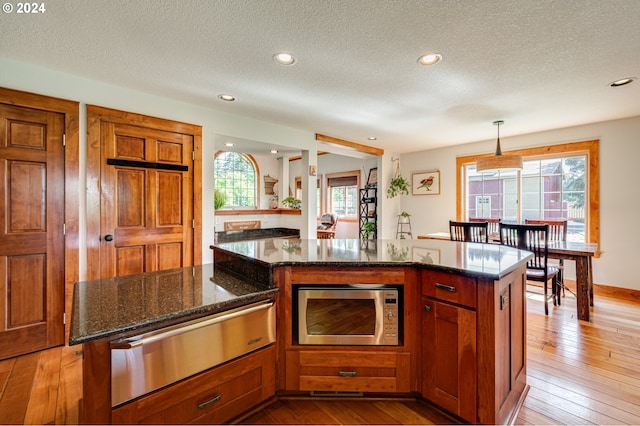 kitchen with a center island, dark stone countertops, plenty of natural light, pendant lighting, and light hardwood / wood-style floors