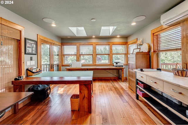 playroom featuring a wall mounted air conditioner, french doors, light wood-type flooring, a skylight, and a textured ceiling