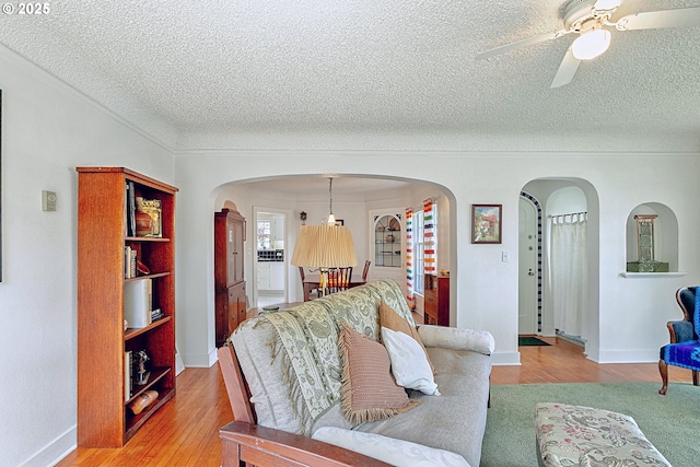 living room featuring arched walkways, ceiling fan, light wood finished floors, and a textured ceiling
